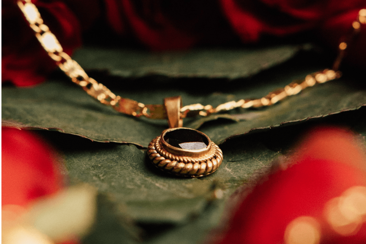 A vintage pendant sits on the leaves of a flower bouquet.