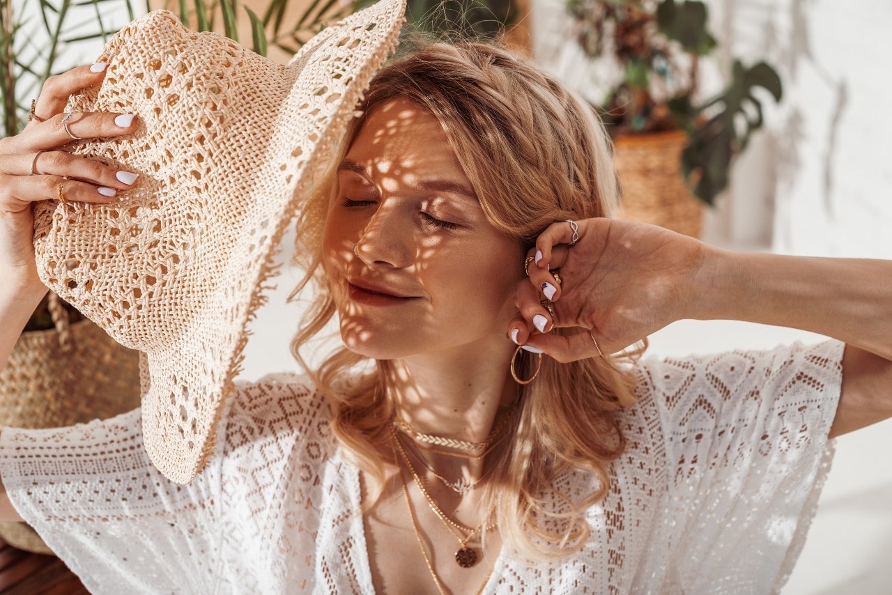 A mother relaxing in the sun on Mother’s Day wearing fine jewelry of gold necklaces, hoop earrings, and rings.